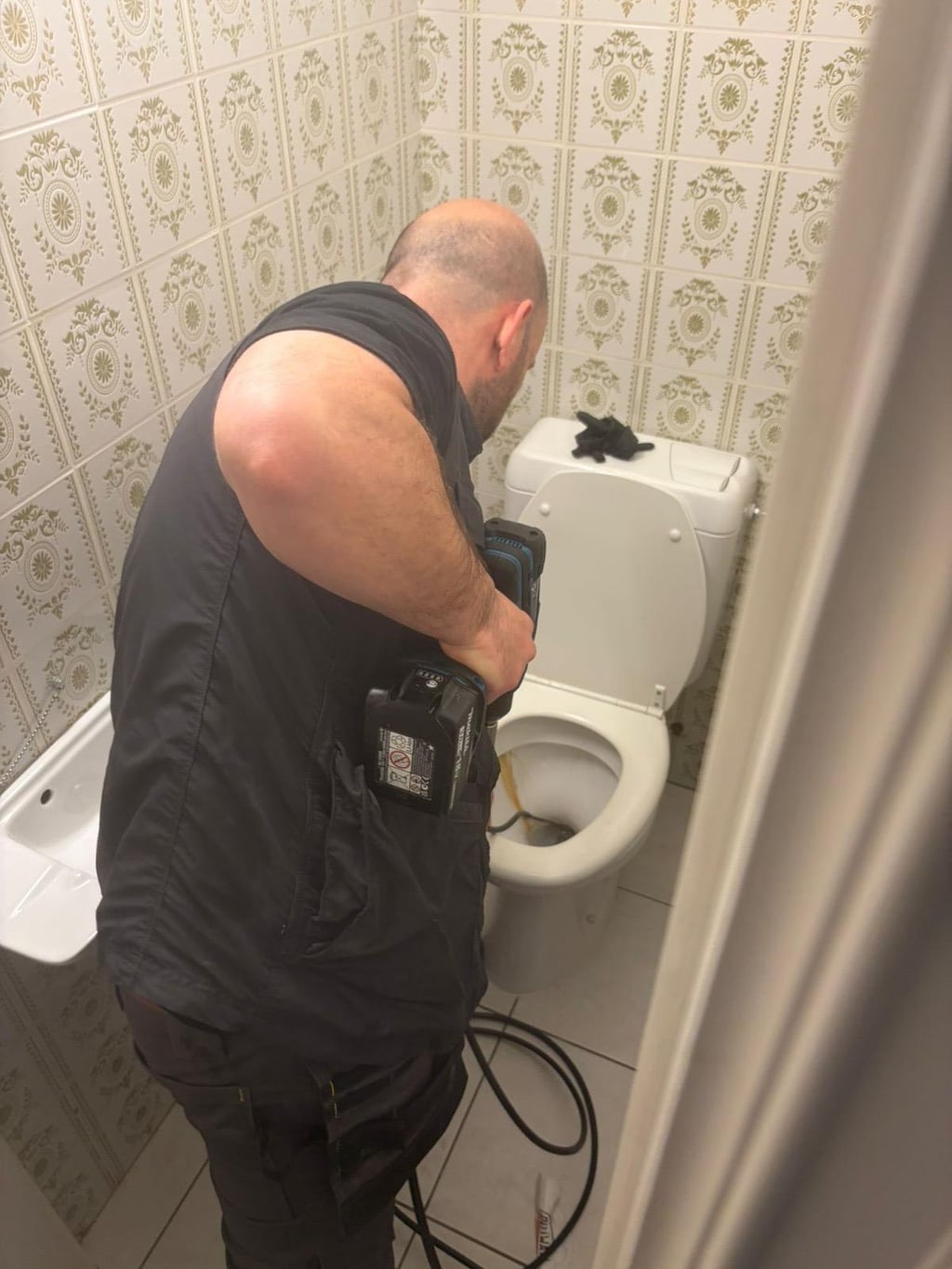 Technicien Nero Canalis utilisant un furet électrique Makita 18V pour déboucher un WC à Watermael-Boitsfort